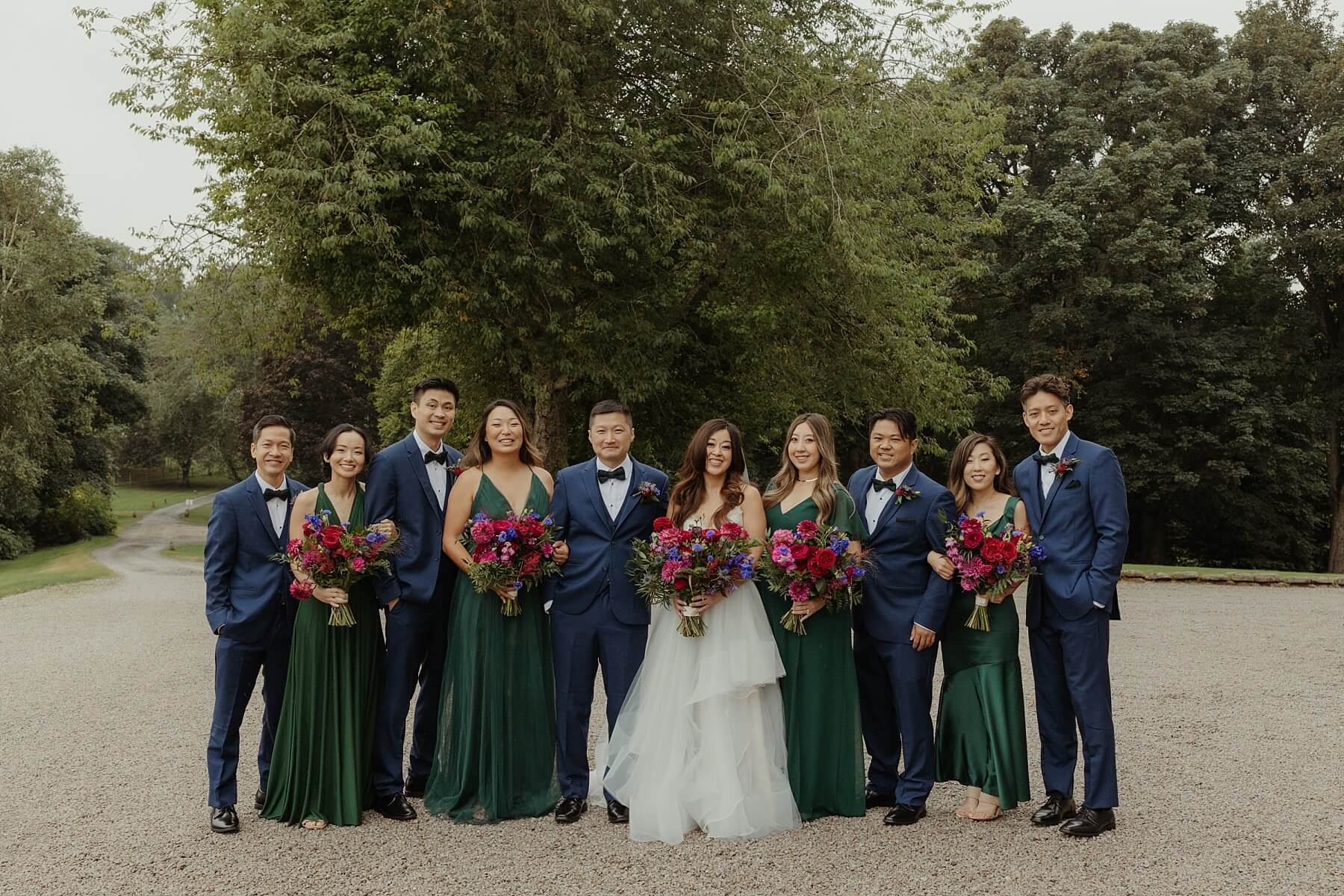 american bride and groom pose with wedding party bridesmaids in green silk dresses and groomsmen in navy suits with bow ties at cluny castle wedding scotland