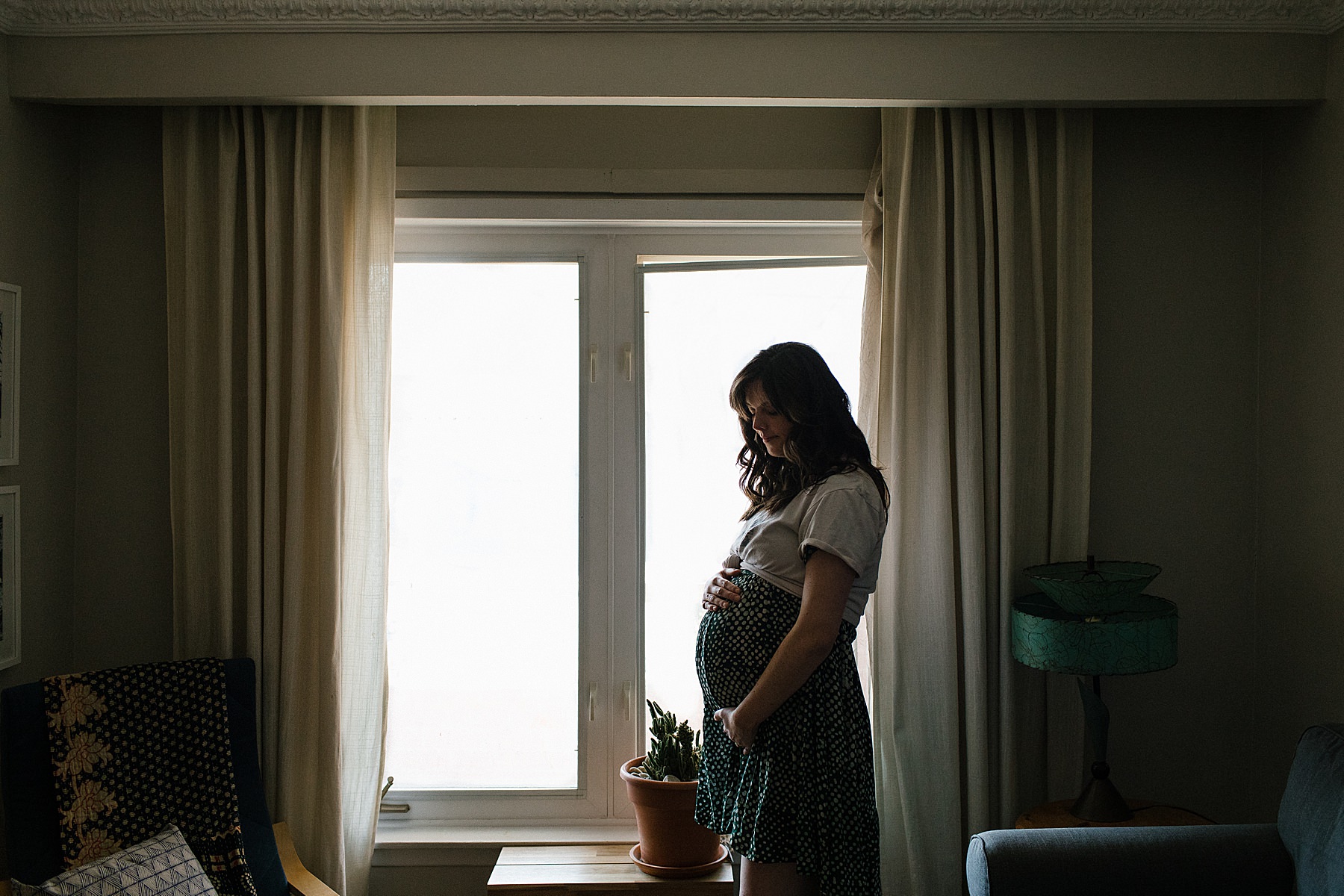 maternity photography toronto pregnancy photoshoot showing a heavily pregnant woman standing by a window holding her baby bump in mississauga GTA ontario