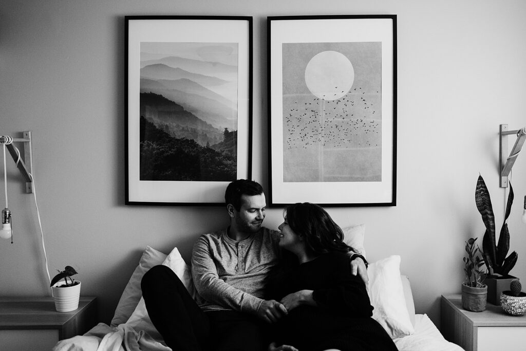 man and pregnant woman pose together on a bed below two framed pictures for maternity photography toronto pregnancy photos